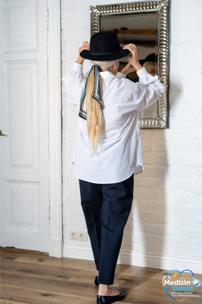 Frau richtet ihren Hut vor dem Spiegel – Symbol für Orientierung, Selbstbestimmung und neue Perspektiven im Gesundheitsweg