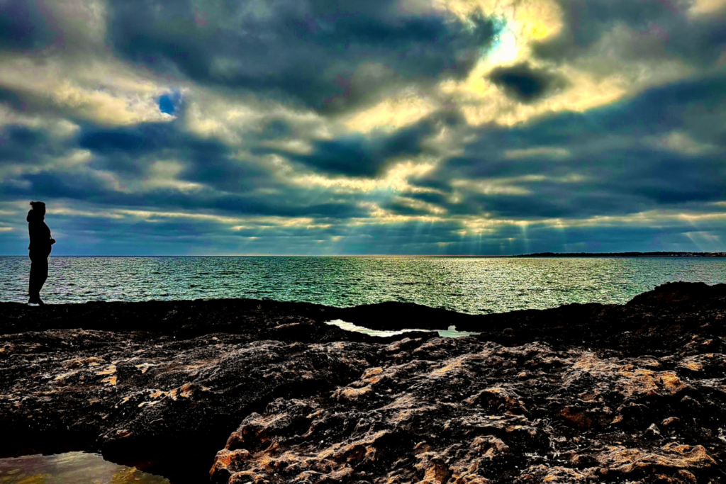 Silhouette einer Person an einer felsigen Küste mit Blick auf das Meer